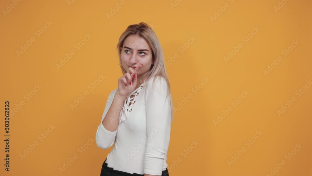 Portrait of cute smiling young woman in pastel white shirt hand prop up on mouth, isolated on orange wall background in studio. People sincere emotions, lifestyle concept. Portrait of cute smiling young woman in pastel white shirt hand prop up on mouth, isolated on orange wall background in studio. People sincere emotions, lifestyle concept.