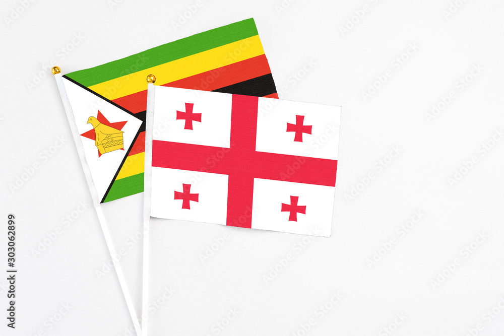 Georgia and Zimbabwe stick flags on white background. High quality fabric, miniature national flag. Peaceful global concept.White floor for copy space.