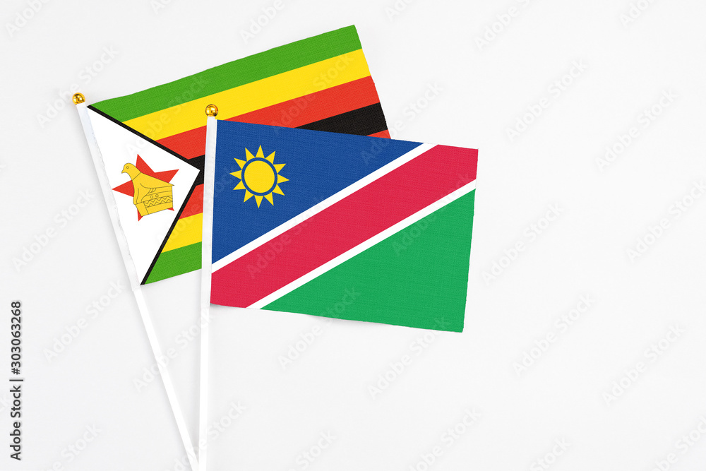 Namibia and Zimbabwe stick flags on white background. High quality fabric, miniature national flag. Peaceful global concept.White floor for copy space. Namibia and Zimbabwe stick flags on white background. High quality fabric, miniature national flag. Peaceful global concept.White floor for copy space.