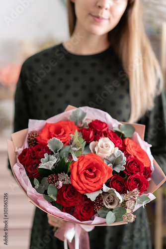 Mixed bouquet of red tones. Beautiful bunch of fresh flowers in womans hands. The work of the florist at a flower shop. Fresh cut flower.