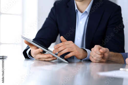 Business people using tablet computer while working together at the desk in modern office. Unknown businessman or male entrepreneur with colleague at workplace. Teamwork and partnership concept