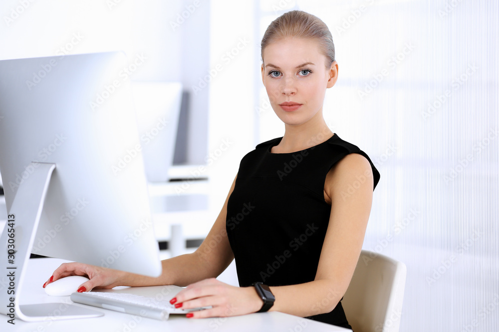 Business woman working with computer while sitting at the desk in modern office. Secretary or female lawyer looks beautiful in black dress. Business people concept Business woman working with computer while sitting at the desk in modern office. Secretary or female lawyer looks beautiful in black dress. Business people concept