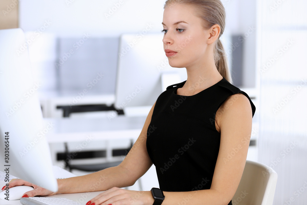 Business woman working with computer while sitting at the desk in modern office. Secretary or female lawyer looks beautiful in black dress. Business people concept Business woman working with computer while sitting at the desk in modern office. Secretary or female lawyer looks beautiful in black dress. Business people concept