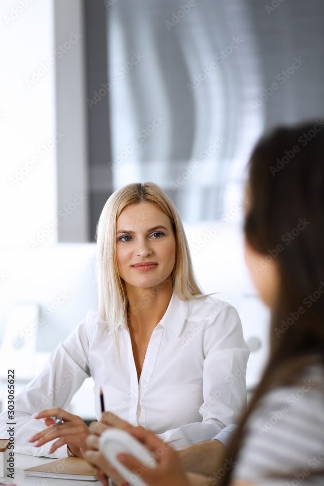 Group of business people discussing questions at meeting. Headshot of blonde businesswoman while smiling to her colleague at office negotiation. Teamwork and cooperation in corporate occupation Group of business people discussing questions at meeting. Headshot of blonde businesswoman while smiling to her colleague at office negotiation. Teamwork and cooperation in corporate occupation