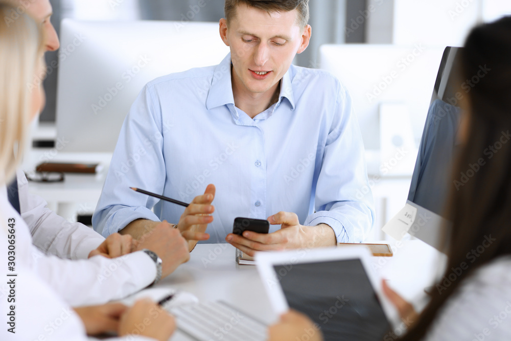 Group of business people discussing questions at meeting. Headshot of casual dressed businessman using smartphone at office negotiation. Teamwork and cooperation in corporate occupation Group of business people discussing questions at meeting. Headshot of casual dressed businessman using smartphone at office negotiation. Teamwork and cooperation in corporate occupation