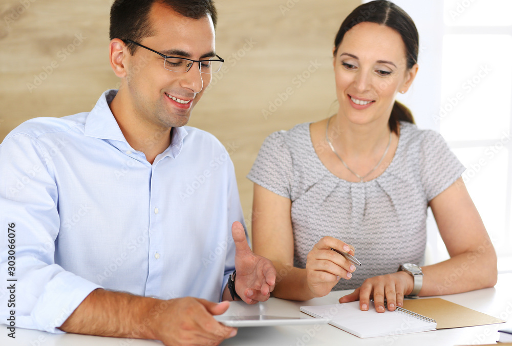 Businessman and hispanic businesswoman using tablet computer in modern office. Headshot of entrepreneur at meeting. Group of diverse people. Teamwork, partnership and business concept Businessman and hispanic businesswoman using tablet computer in modern office. Headshot of entrepreneur at meeting. Group of diverse people. Teamwork, partnership and business concept