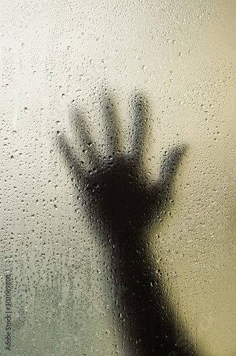 Fototapeta Naklejka Na Ścianę i Meble -  The shadow of a human hand behind a glass with water droplets