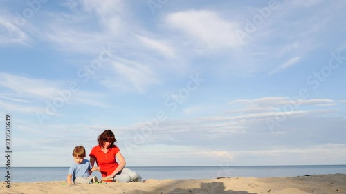 Mother playing with little child boy on sand beach. Adult woman and her son enjoying summer day on seshore. Family holiday at sea. Slow motion photo