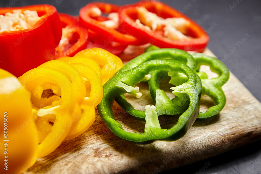 Slices of red, green, and yellow bell peppers on a wooden cutting board, closeup. Sliced sweet peppers in different colors, vegetable salad ingredient, cooking healthy food Slices of red, green, and yellow bell peppers on a wooden cutting board, closeup. Sliced sweet peppers in different colors, vegetable salad ingredient, cooking healthy food
