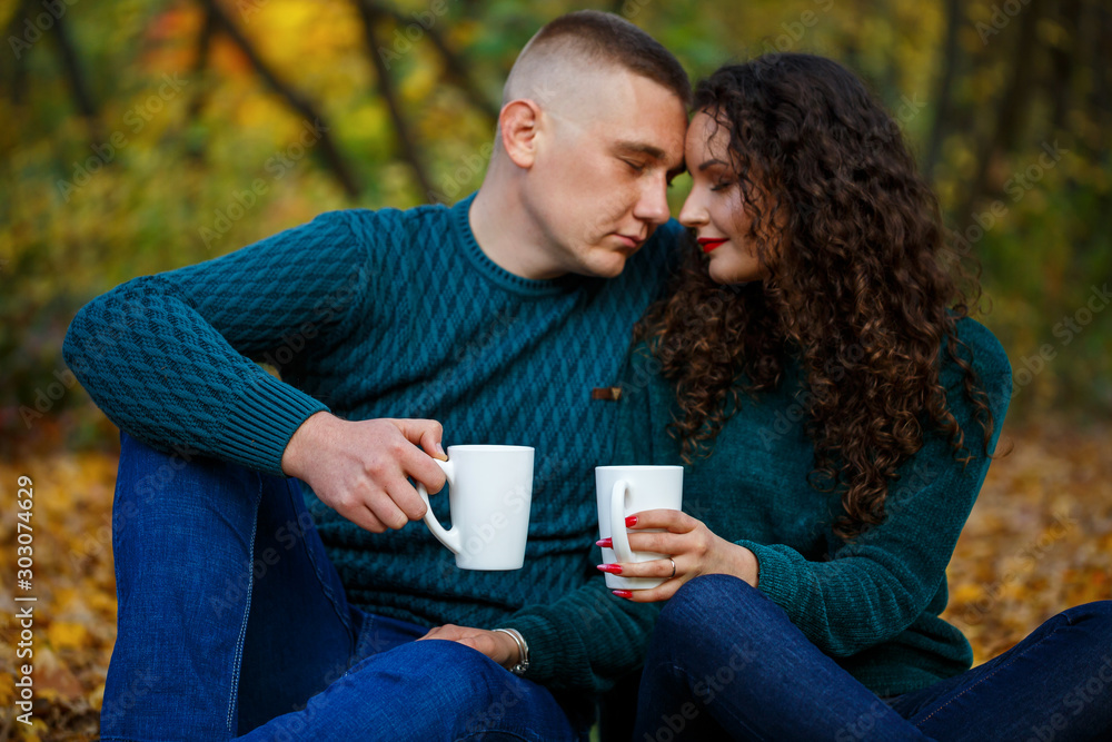 Couple in sweaters drinks tea in the autumn forest Couple in sweaters drinks tea in the autumn forest