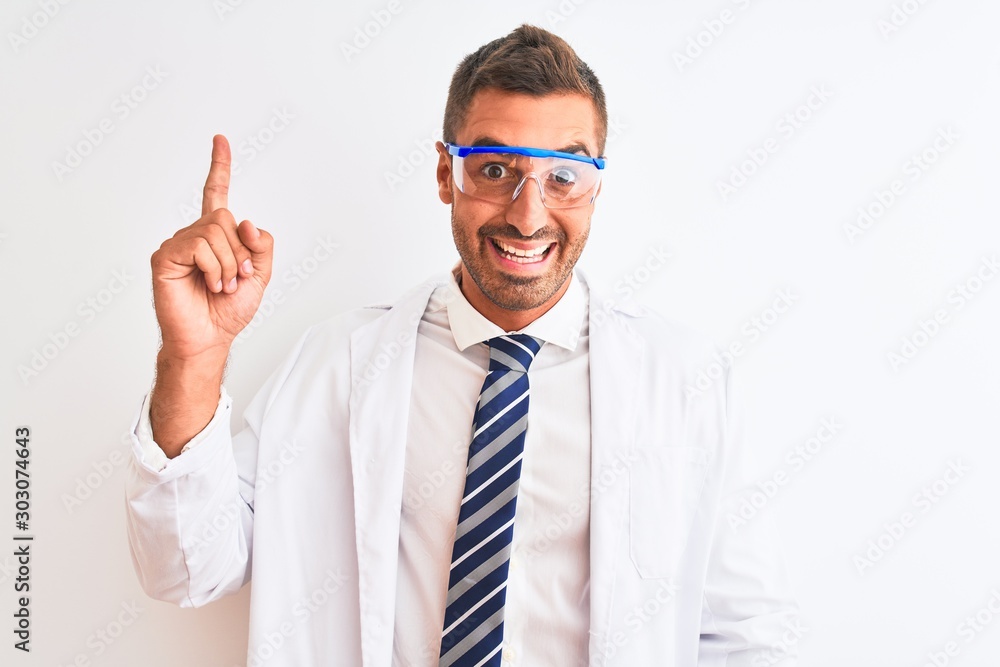 Young handsome scientist man wearing safety glasses over isolated background pointing finger up with successful idea. Exited and happy. Number one. Young handsome scientist man wearing safety glasses over isolated background pointing finger up with successful idea. Exited and happy. Number one.