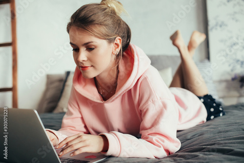 фотографія Calm and concentrated young woman lying on stomach on bed alone