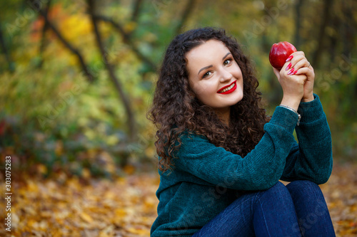 girl in a green sweater and an apple in her hands in the autumn forest