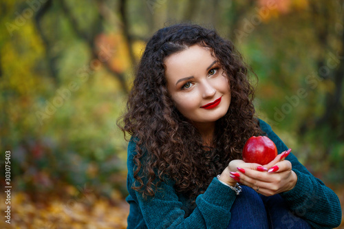 girl in a green sweater and an apple in her hands in the autumn forest