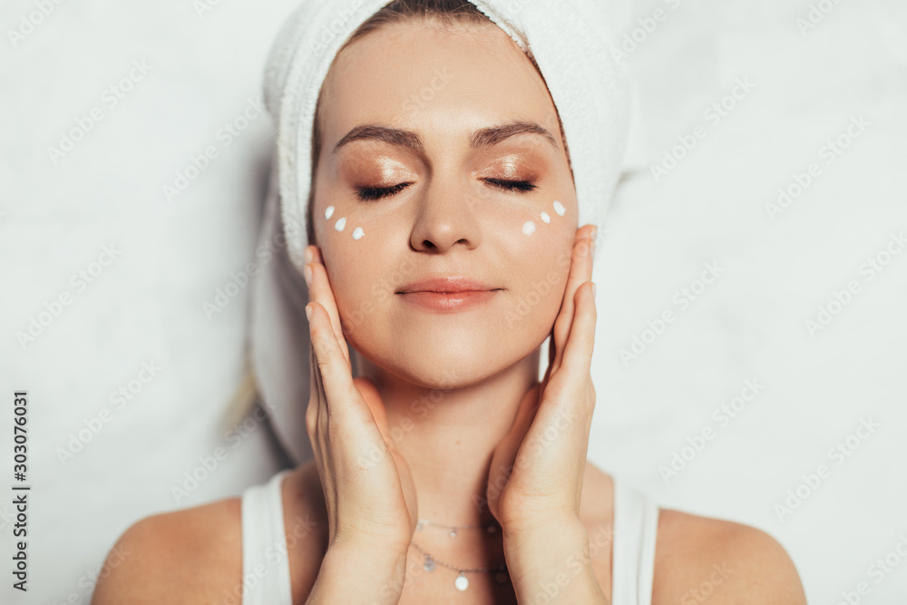 Portrait of natural beauty. Young nice attractive woman isolated over grey background. Has some cream spots on face. Clear skin without acne. Touching face with fingers. Beauty routine. Portrait of natural beauty. Young nice attractive woman isolated over grey background. Has some cream spots on face. Clear skin without acne. Touching face with fingers. Beauty routine.