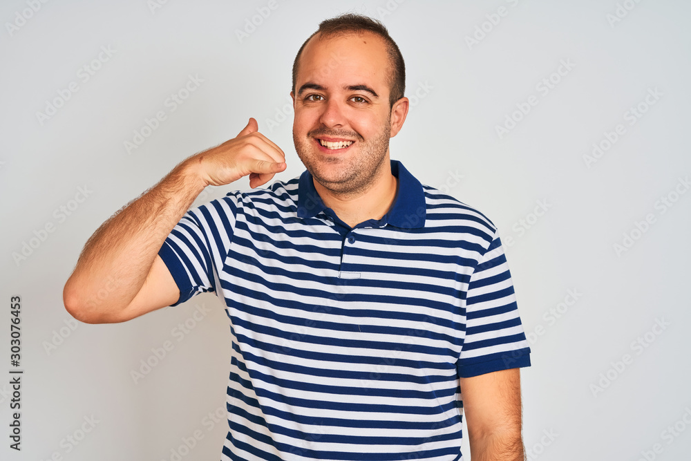 Young man wearing casual striped polo standing over isolated white background smiling doing phone gesture with hand and fingers like talking on the telephone. Communicating concepts. Young man wearing casual striped polo standing over isolated white background smiling doing phone gesture with hand and fingers like talking on the telephone. Communicating concepts.