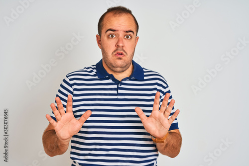 Young man wearing casual striped polo standing over isolated white background Moving away hands palms showing refusal and denial with afraid and disgusting expression. Stop and forbidden.