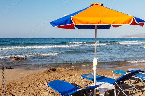 Beach on the Mediterranean coast. Yellow and blue umbrella, sun loungers on the beach with the incoming wave