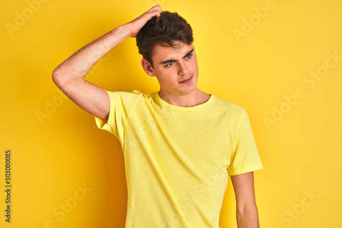 Teenager boy wearing yellow t-shirt over isolated background confuse and wonder about question. Uncertain with doubt, thinking with hand on head. Pensive concept.