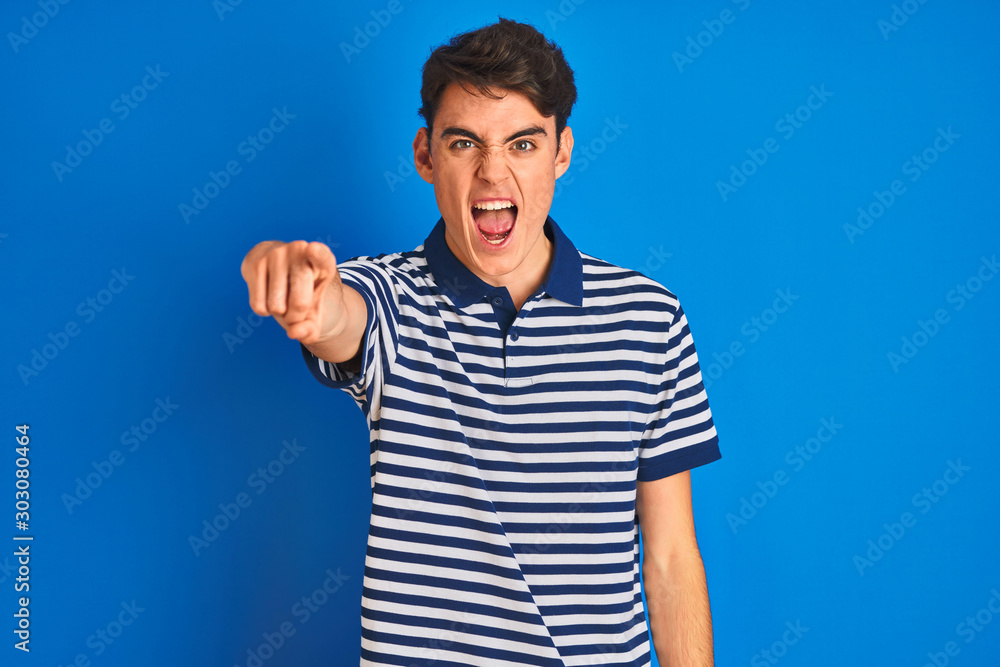Teenager boy wearing casual t-shirt standing over blue isolated background pointing displeased and frustrated to the camera, angry and furious with you Teenager boy wearing casual t-shirt standing over blue isolated background pointing displeased and frustrated to the camera, angry and furious with you