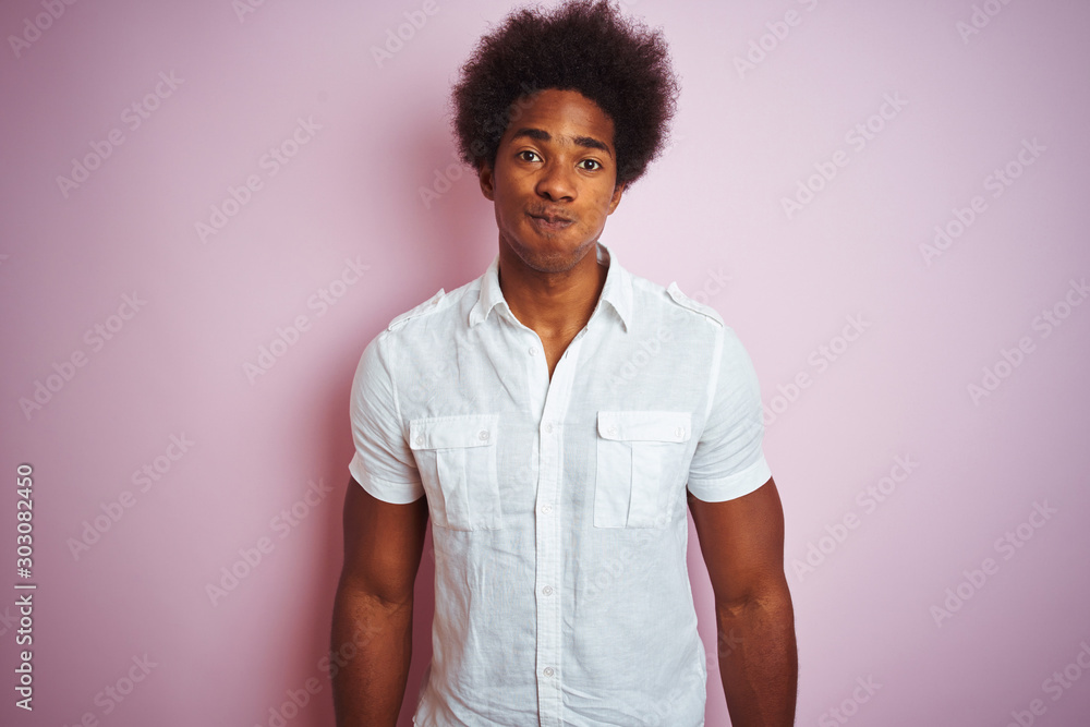 Young american man with afro hair wearing white shirt standing over isolated pink background puffing cheeks with funny face. Mouth inflated with air, crazy expression. Young american man with afro hair wearing white shirt standing over isolated pink background puffing cheeks with funny face. Mouth inflated with air, crazy expression.