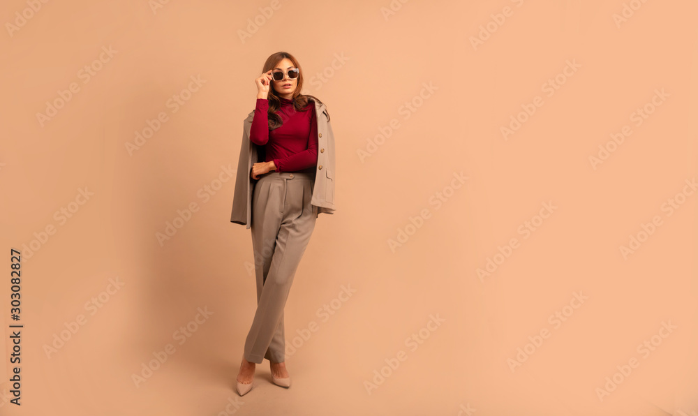 Full length studio portrait of young business woman. Full length portrait of smiling attractive businesswoman in suit posing while standing with arms crossed and looking at camera isolated over beige Full length studio portrait of young business woman. Full length portrait of smiling attractive businesswoman in suit posing while standing with arms crossed and looking at camera isolated over beige