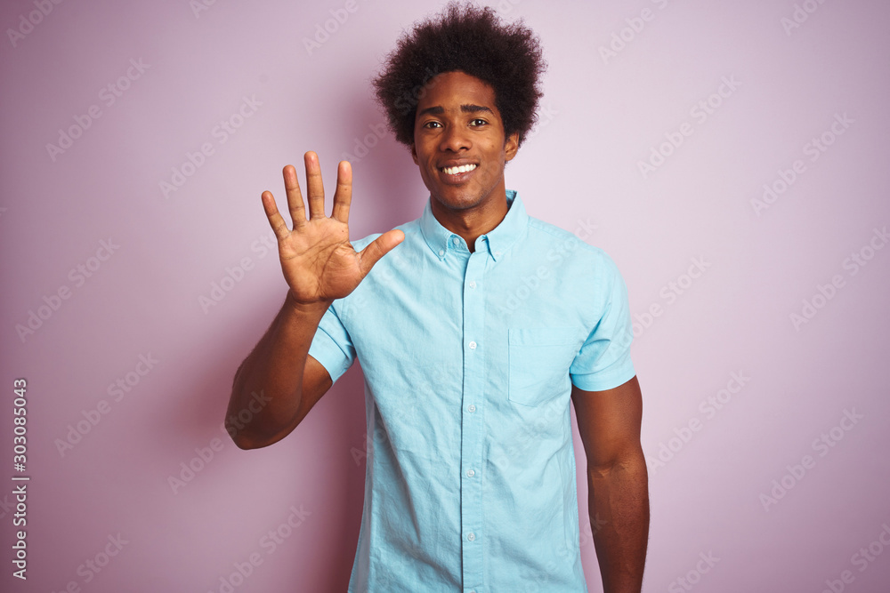 Young american man with afro hair wearing blue shirt standing over isolated pink background showing and pointing up with fingers number five while smiling confident and happy. Young american man with afro hair wearing blue shirt standing over isolated pink background showing and pointing up with fingers number five while smiling confident and happy.