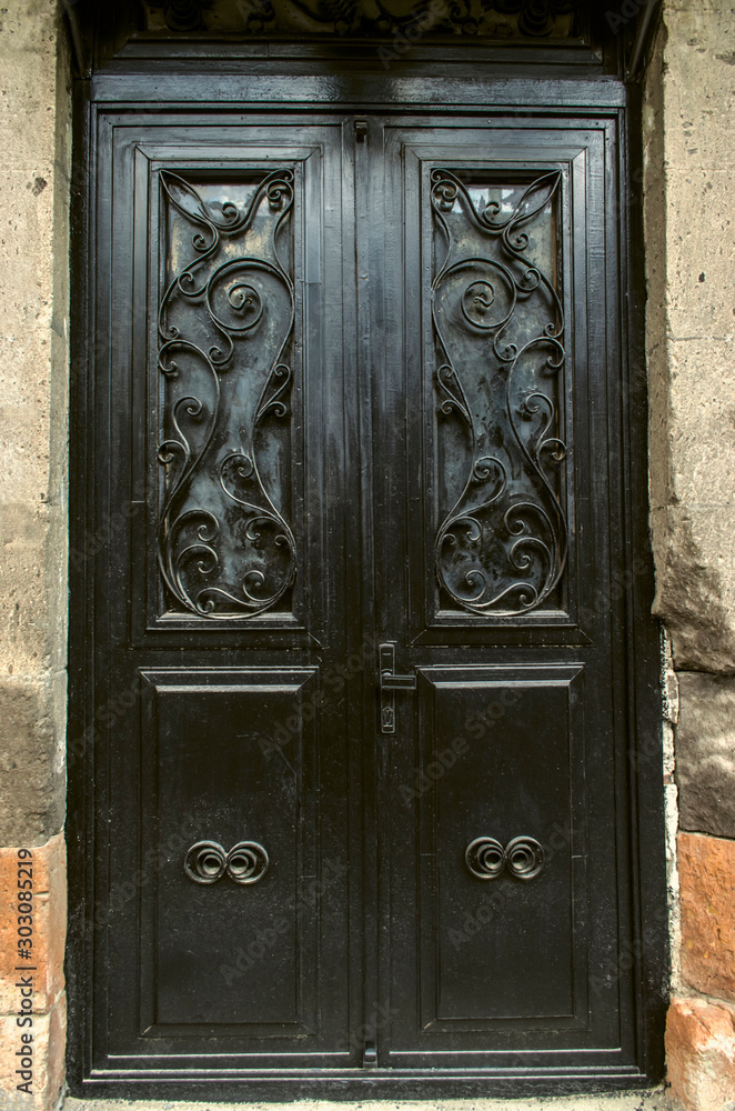Black double leaf iron door covered with wrought iron decorative black bars on the facade of a stone building