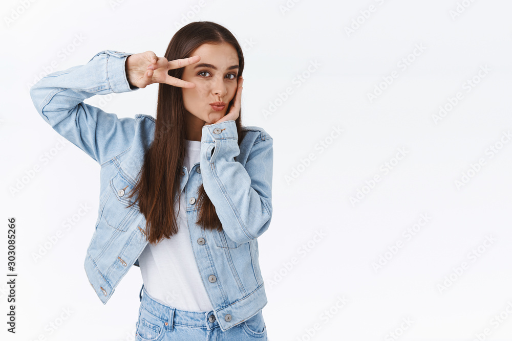 Coquettish, feminine good-looking brunette woman in denim outfit, showing peace or victory sign over eye, tilt head and pouting flirty, smiling as making tender, cute grimaces, white background Coquettish, feminine good-looking brunette woman in denim outfit, showing peace or victory sign over eye, tilt head and pouting flirty, smiling as making tender, cute grimaces, white background