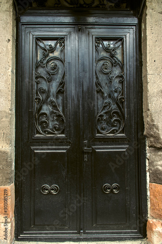 Black double leaf iron door covered with wrought iron decorative black bars on the facade of a stone building