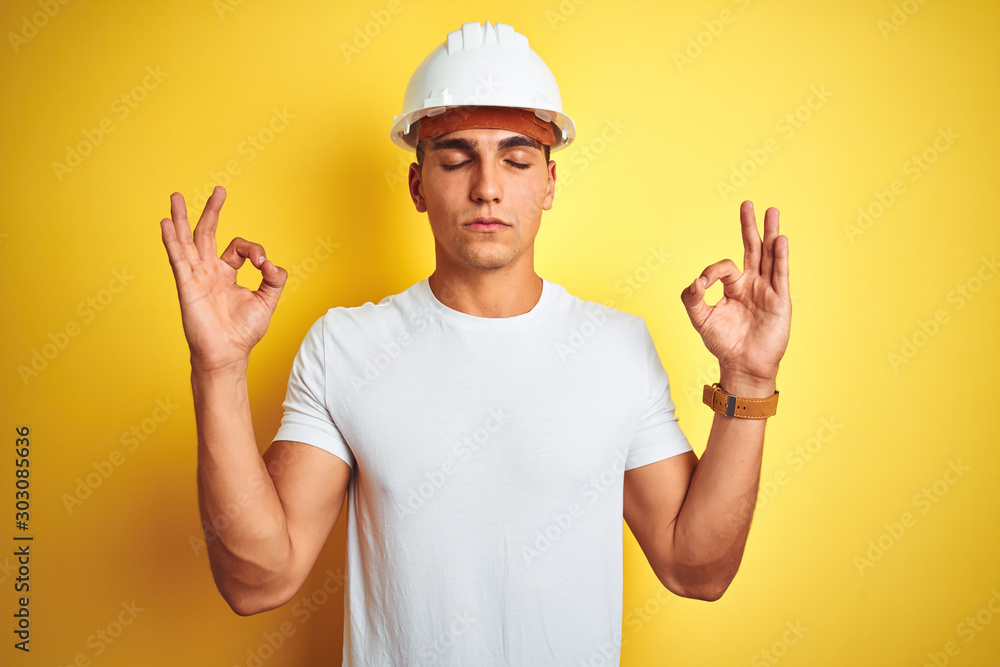 Young handsome man wearing construction helmet over yellow isolated background relax and smiling with eyes closed doing meditation gesture with fingers. Yoga concept.