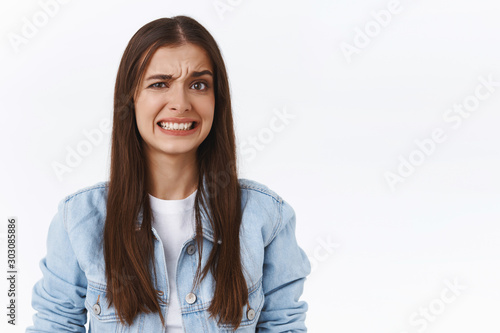 Girl cringe as seeing something embarrassing and bothering. Woman make uncomfortable smile and squinting feeling worried and displeased, see bothering bad situation, standing white background photo