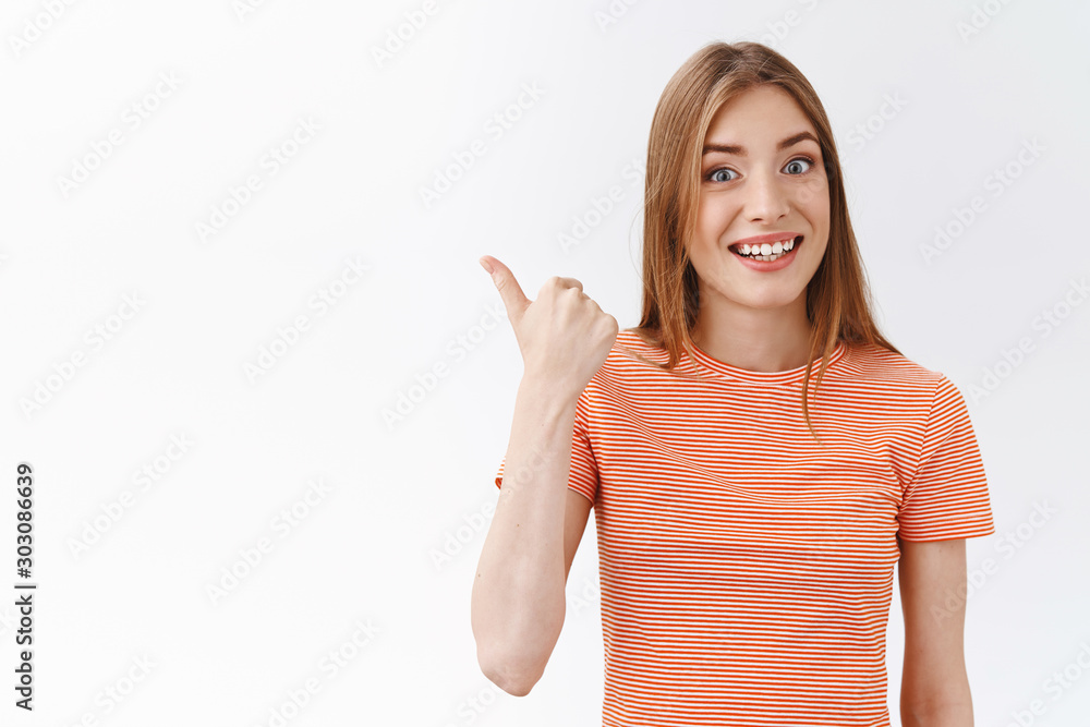 Waist-up attractive, cheerful young caucasian woman in striped t-shirt smiling amused and enthusiastic, pointing left with thumb, invite take look interesting promo, standing white background Waist-up attractive, cheerful young caucasian woman in striped t-shirt smiling amused and enthusiastic, pointing left with thumb, invite take look interesting promo, standing white background