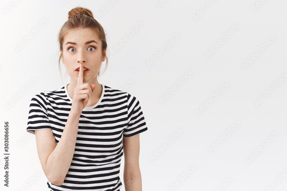 Shhh dont say word. Excited young silly girl with bun wear striped t-shirt, press finger to lips seal with promise not tell anybody, hiding secret, gossiping behind coworker back, white background Shhh dont say word. Excited young silly girl with bun wear striped t-shirt, press finger to lips seal with promise not tell anybody, hiding secret, gossiping behind coworker back, white background