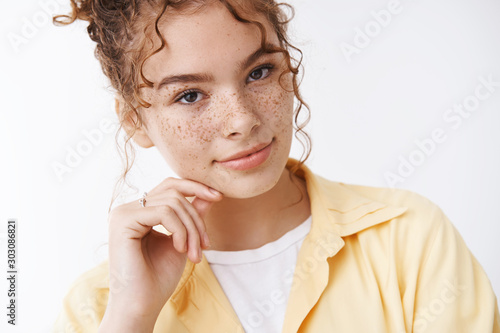 Close-up tender feminine young 20s female university student redhead freckles cheeks smiling gently touch cheek tilting head expressin sensuality, flirting standing white background photo