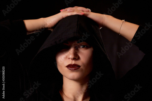 Monochrome image of a hooded woman on a dark background.