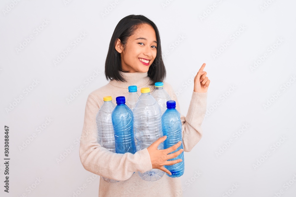 Young beautiful chinese woman recycling plastic bottles over isolated white background very happy pointing with hand and finger to the side Young beautiful chinese woman recycling plastic bottles over isolated white background very happy pointing with hand and finger to the side