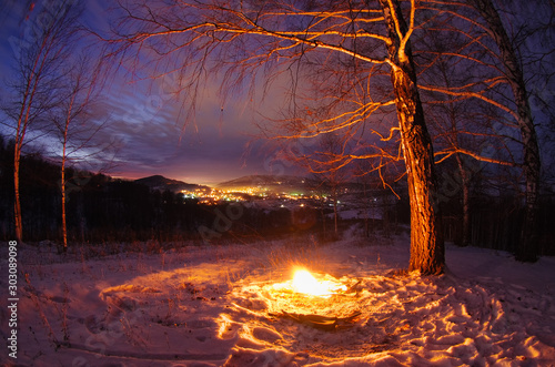 Night fire on the mountain on the background of the bright sunset town village under a dark sky