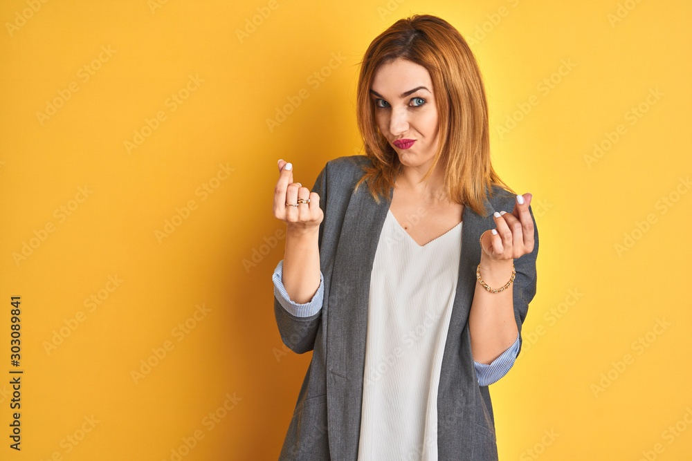 Redhead caucasian business woman over yellow isolated background doing money gesture with hands, asking for salary payment, millionaire business Redhead caucasian business woman over yellow isolated background doing money gesture with hands, asking for salary payment, millionaire business