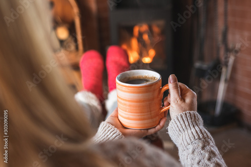 Woman is drinking hot coffee and sitting in front of fireplace