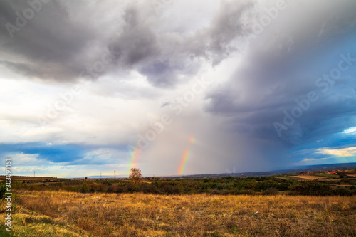 Rainbow in a dark clouds above the meadow