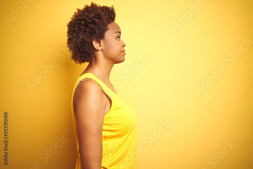 Beauitul african american woman wearing summer t-shirt over isolated yellow background looking to side, relax profile pose with natural face with confident smile.