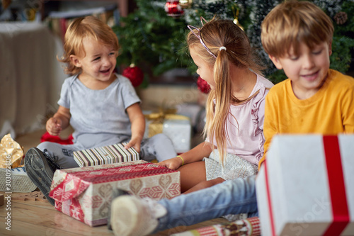 Cute kids opening Christmas gift at home.