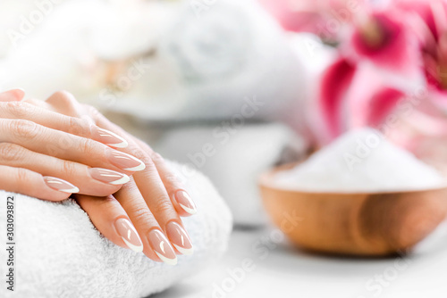 Luxury nails french manicure concept. Woman in cosmetics salon with towels, salt in olive bowl and flowers in background. Relaxing hands massage or spa treatment procedure.