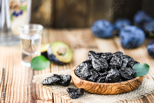 Prunes in bowl  and green leaf. Slivovitz or alcohol brandy bottle and small glass with fresh plume in background.