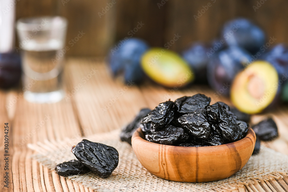 Prunes in wooden bowl on rustic table. Plums and brandy or slivovitz in small glass background. Prunes in wooden bowl on rustic table. Plums and brandy or slivovitz in small glass background.