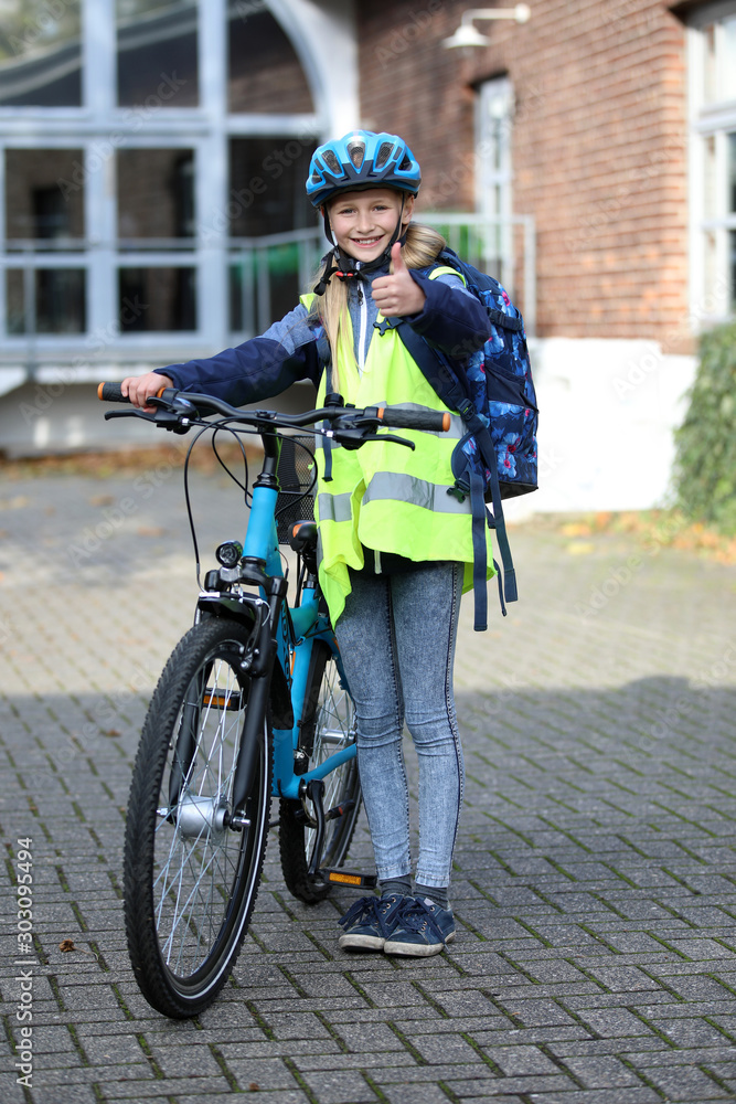 Schulkind mit Fahrrad, trägt Helm und Warnweste und zeigt Daumen