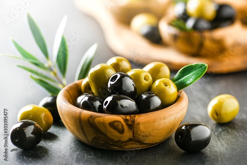 Canvastavla Fresh olives with core in olive bowl on dark stone table and green leaves