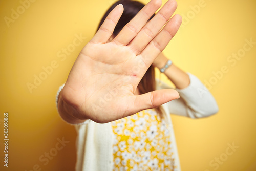 Young beautiful woman wearing jacket standing over yellow isolated background covering eyes with hands and doing stop gesture with sad and fear expression. Embarrassed and negative concept.