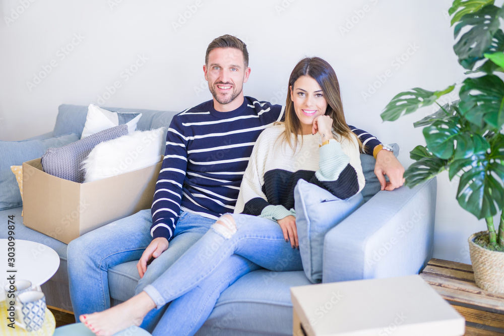 Young beautiful couple sitting on the sofa drinking cup of coffee at new home around cardboard boxes Young beautiful couple sitting on the sofa drinking cup of coffee at new home around cardboard boxes